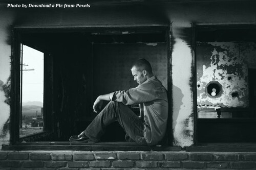 sad man sitting against concrete column